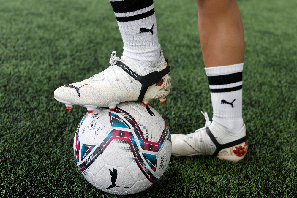 Person wearing Puma soccer cleats and socks with a soccer ball on grass and wearing Playermaker Smart Soccer Tracker.